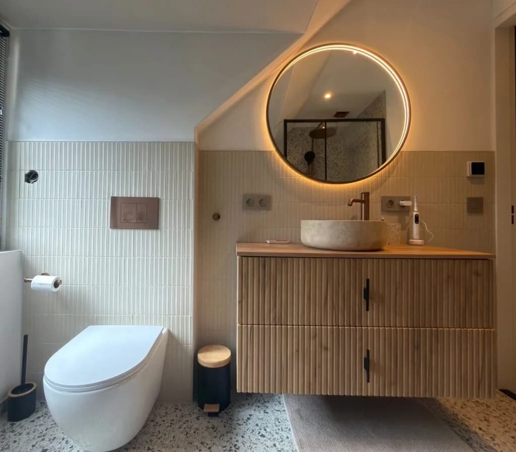 Badkamer met ronde verlichte spiegel, waskom en hangend toilet