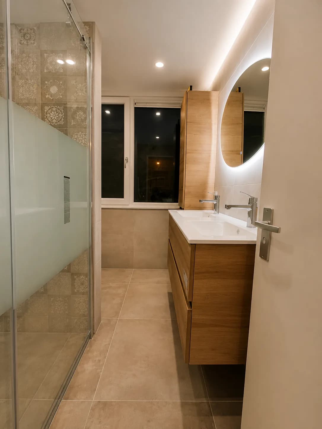 Badkamer met glazen douchewand, patroontegels en een houten wastafelmeubel